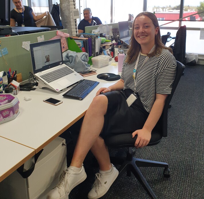 A young woman, Kaitlin, sits at her desk in the Aviva office smiling