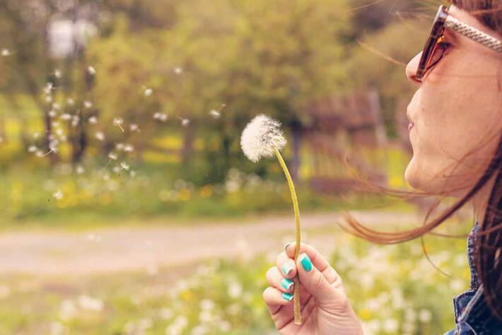 Woman making a wish by blowing on a dandelion